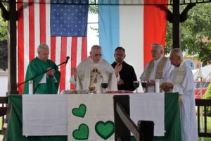 Priest at alter with other religious figures standing around him.