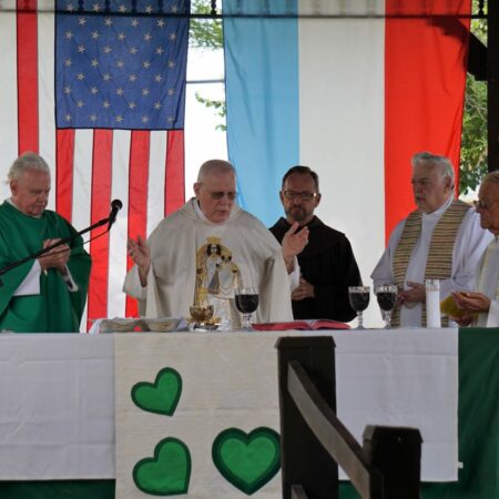 Priest at alter with other religious figures standing around him.