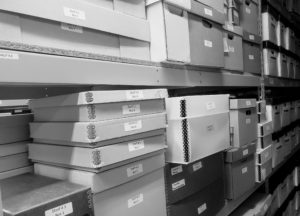 Black, white, and grey archival boxes stacked on shelves.